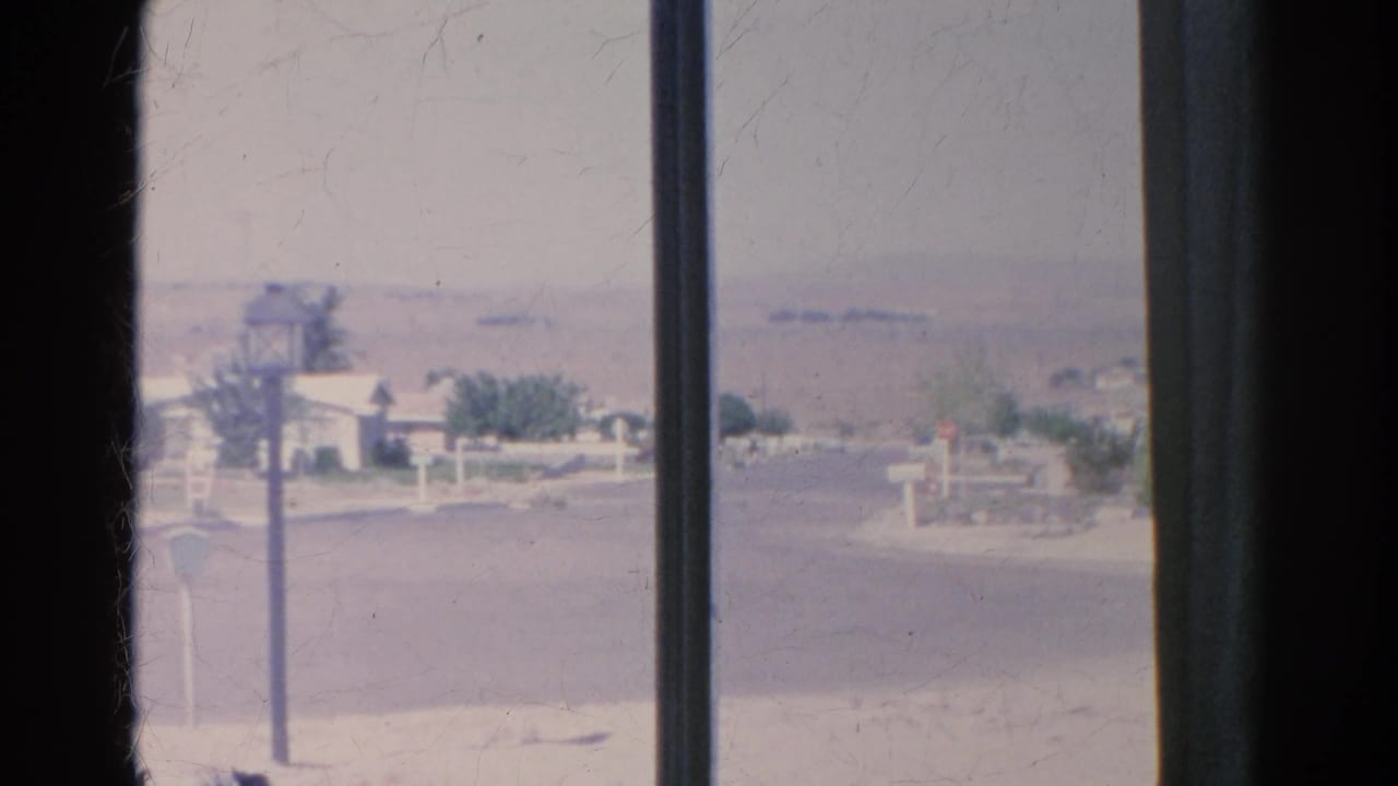 1966 8mm Silver Lake, California view through a house window toward a quiet road, mailboxes, a lamppost, low homes, and hazy hills.