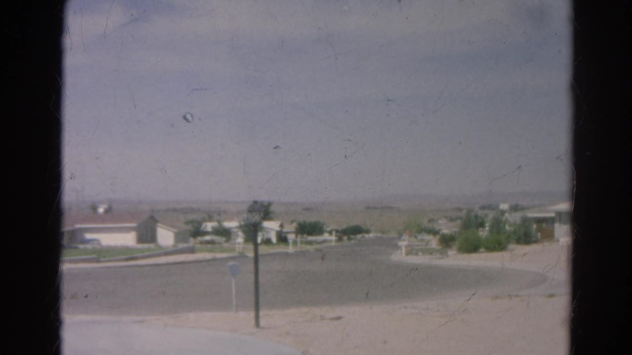 1966 8mm view of a Silver Lake cul-de-sac with single-story homes, sparse landscaping, posts, and distant hazy hills.