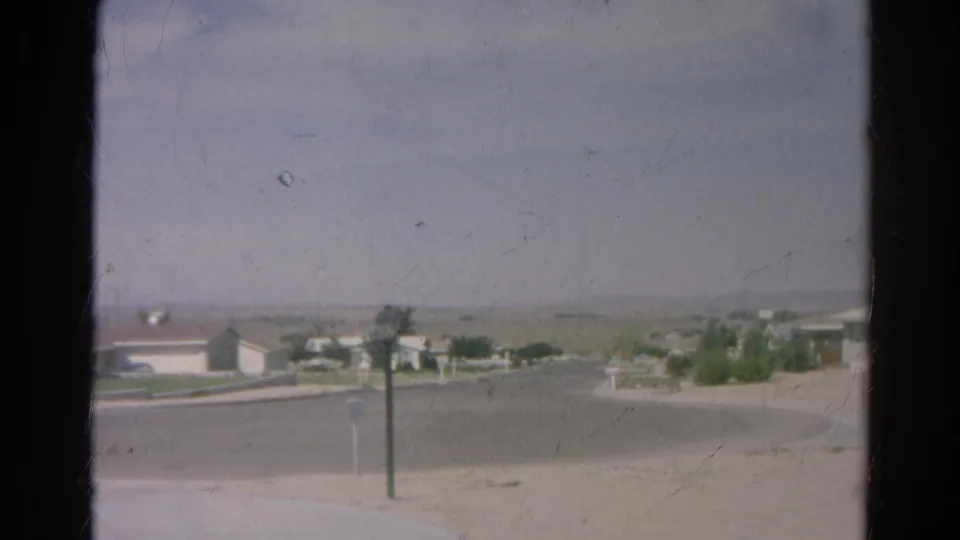 1966 8mm view of a Silver Lake cul-de-sac with single-story homes, sparse landscaping, posts, and distant hazy hills.