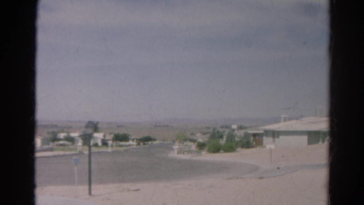 A soft 8mm frame of the Silver Lake cul-de-sac shows dry ground, a roadside post, low homes, and hazy hills in the distance.