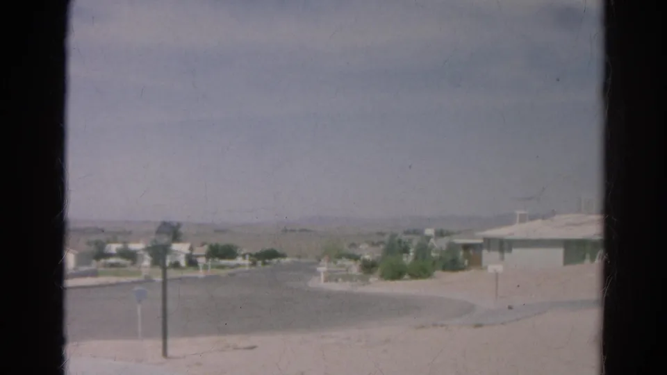 A soft 8mm frame of the Silver Lake cul-de-sac shows dry ground, a roadside post, low homes, and hazy hills in the distance.