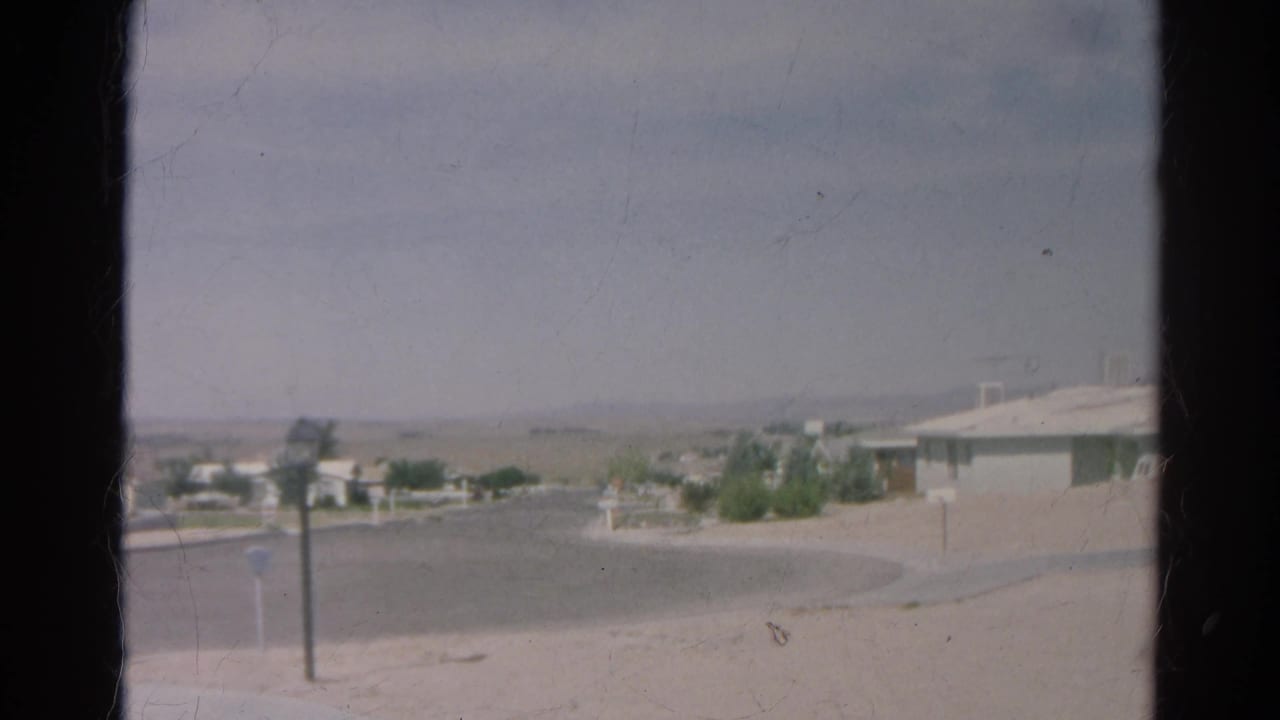 Final 1966 Silver Lake frame showing the edge of a low house, curved street, posts, sparse landscaping, and a hazy hillside backdrop.