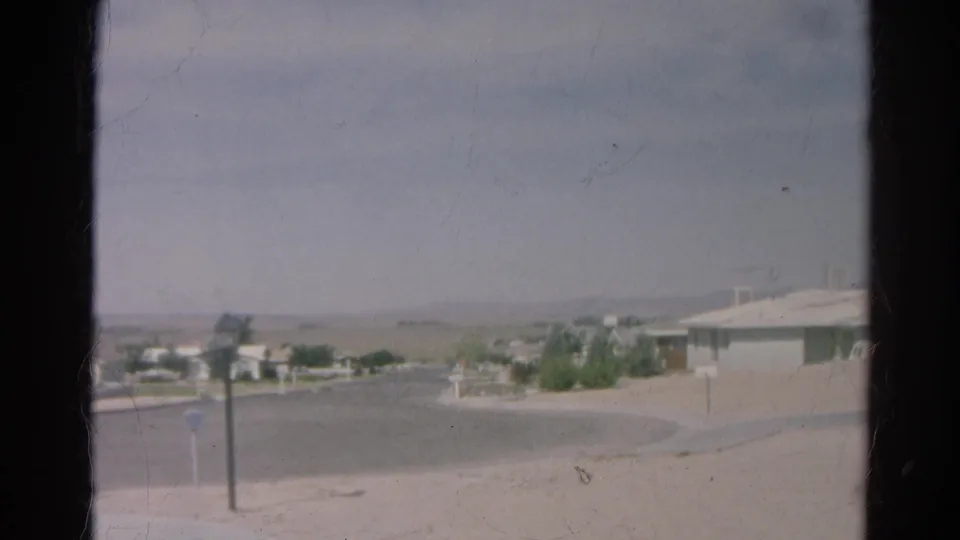 Final 1966 Silver Lake frame showing the edge of a low house, curved street, posts, sparse landscaping, and a hazy hillside backdrop.