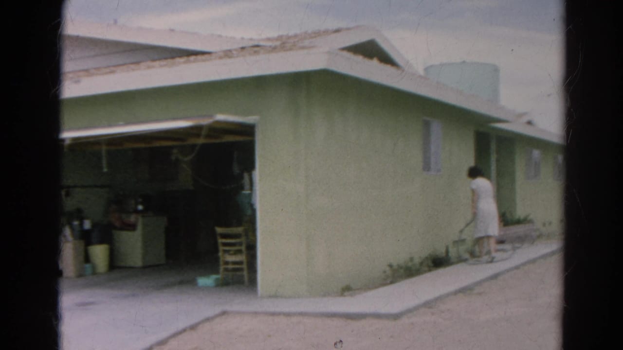 1966 Silver Lake frame showing a woman in a white dress beside a pale green house near an open garage and side walkway.