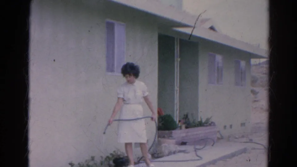 The woman waters near a low planter beside the green stucco home in Silver Lake, California.