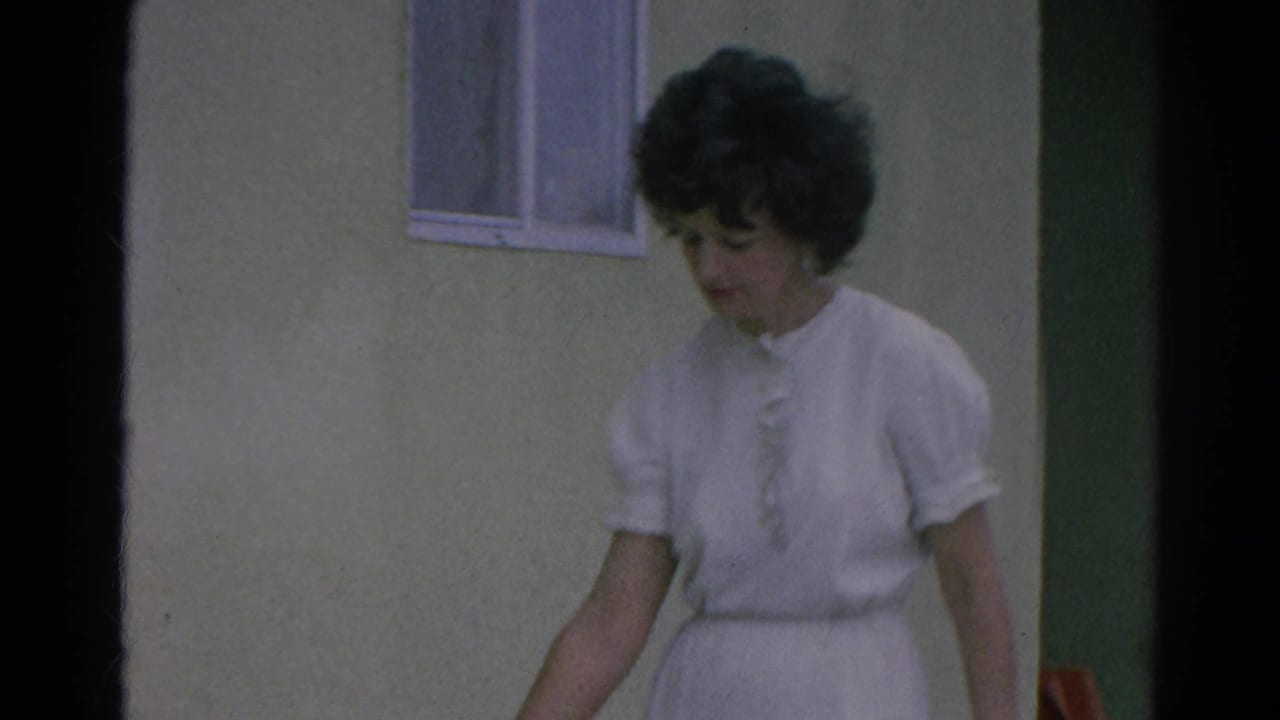 Closer 1966 view of the woman in a white dress near the stucco wall, window, and shaded doorway.