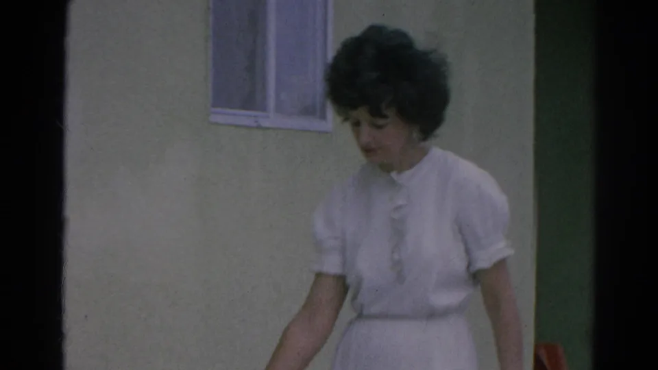 Closer 1966 view of the woman in a white dress near the stucco wall, window, and shaded doorway.