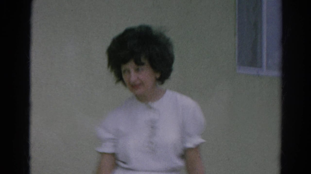 The woman faces the camera near the green stucco wall and window in the Silver Lake home-movie scene.