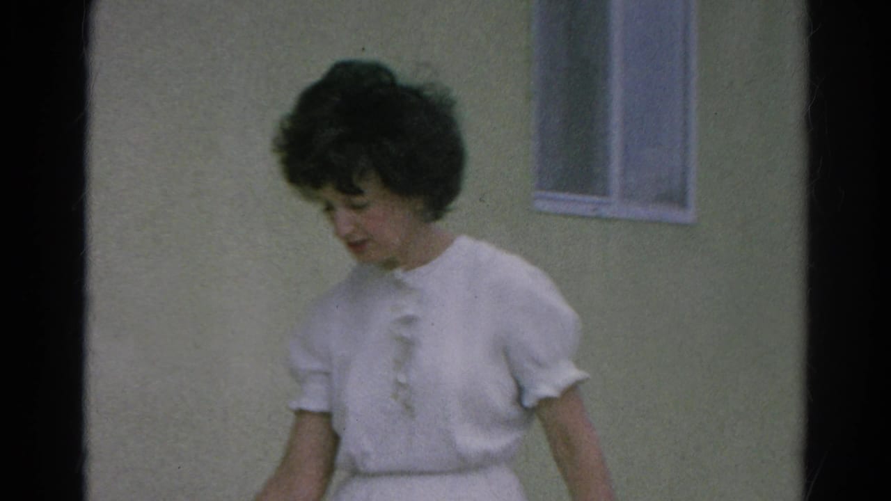 Woman in white blouse looking downward outside a simple building.