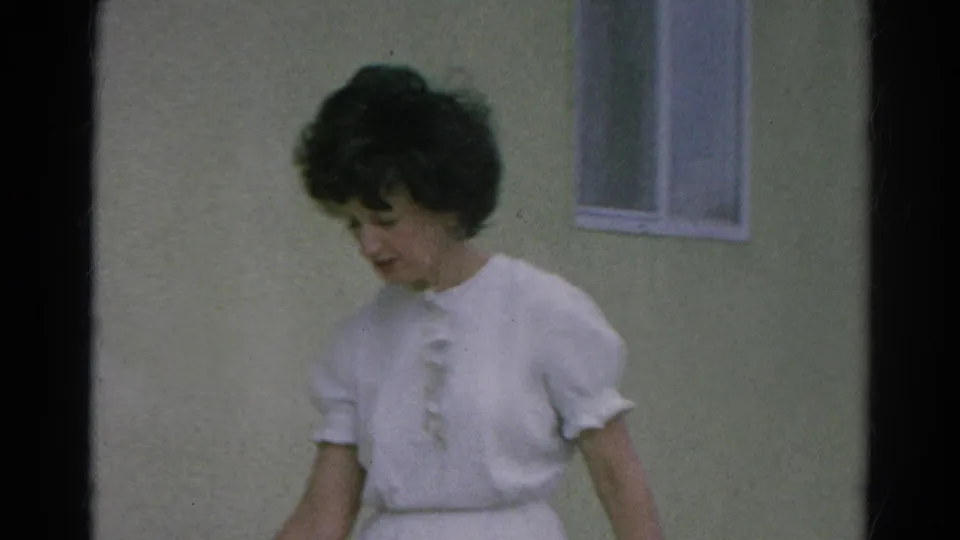A woman in mid-1960s dress looks down while standing outside a modest building in Silver Lake, California.