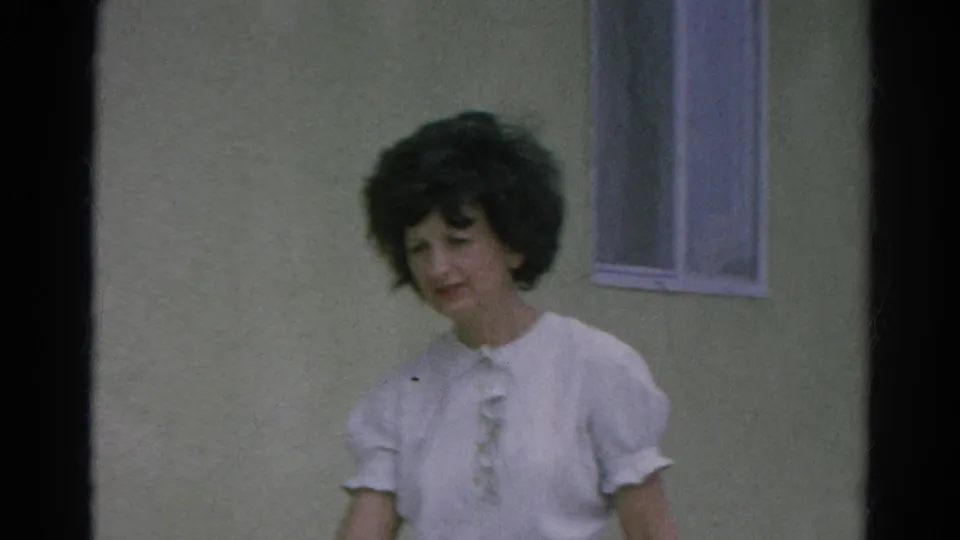 Closer home-movie view of a woman in a white ruffled blouse beside a small window in 1966 Silver Lake, California.