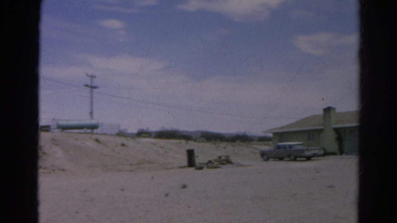 Wide 1966 Silver Lake roadside view with a dirt road, utility pole, parked vintage car, low building, and cloudy sky.