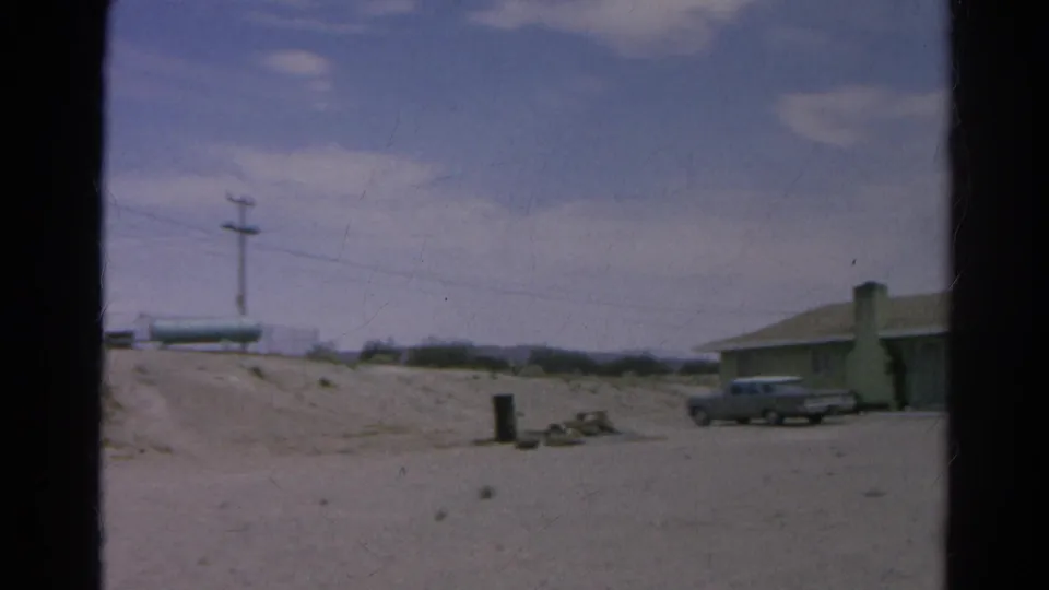 Wide 1966 Silver Lake roadside view with a dirt road, utility pole, parked vintage car, low building, and cloudy sky.