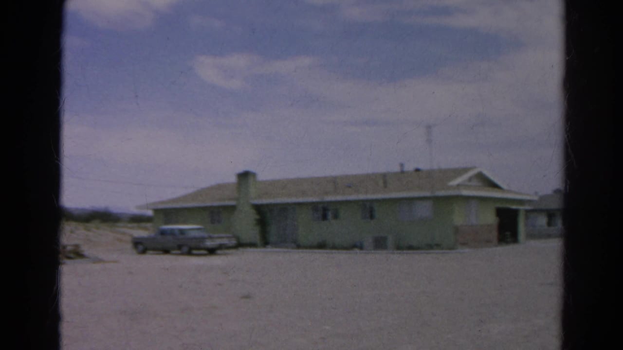 Final 1966 Silver Lake frame shows a wider view of the low house, parked silver sedan, chimney, sandy lot, and darker doorway at the right edge.