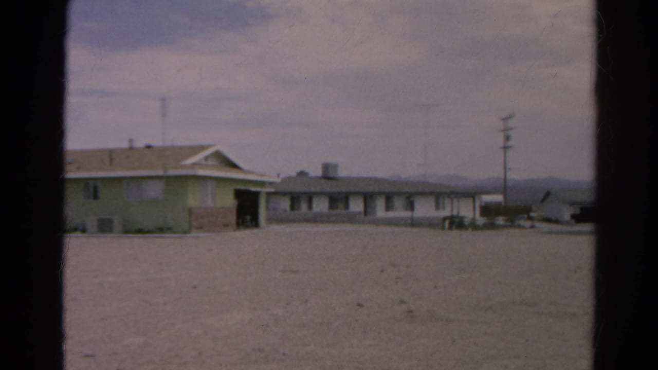 1966 Silver Lake frame with the roadside building partly cropped, a utility pole, gravel lot, and distant desert hills.
