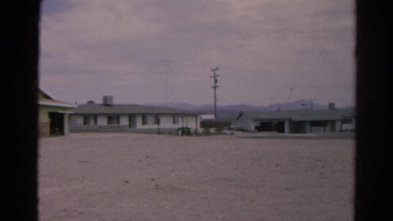 Low flat-roof buildings across a gravel lot with utility poles and distant mountains.