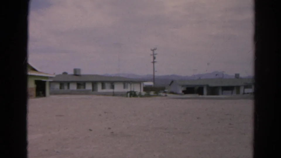 1966 Silver Lake, California view of low roadside buildings beyond a gravel lot, with utility poles and mountains under a pale sky.