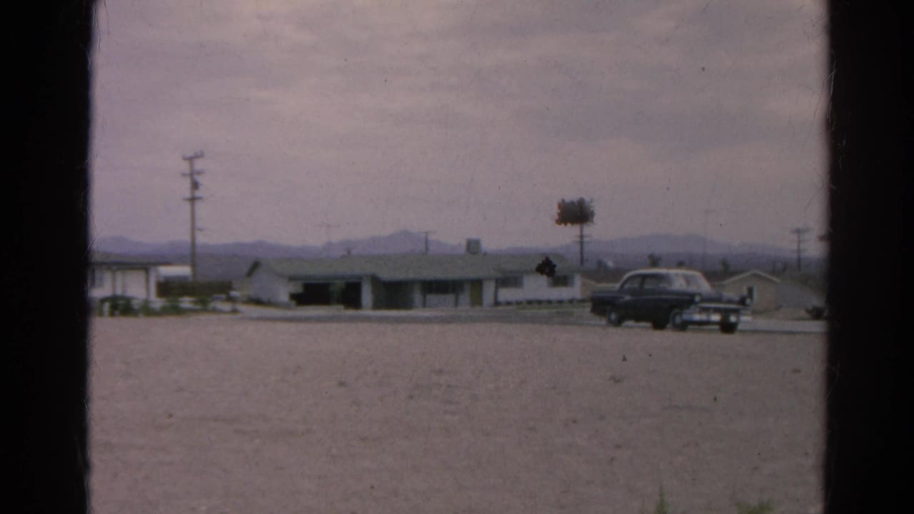 1966 Silver Lake, California frame showing a dark sedan near low flat-roof buildings, a utility pole, gravel foreground, and distant mountains.