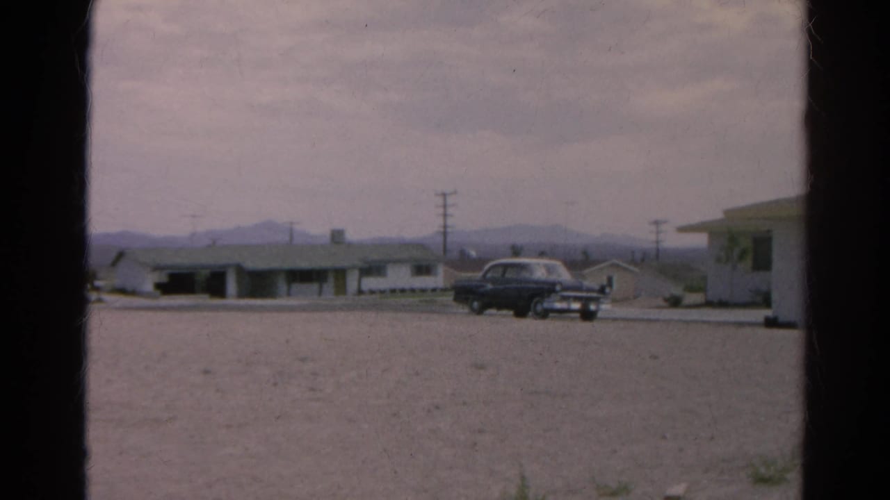 1966 Silver Lake, California roadside scene with a dark sedan, low motel-like buildings, utility poles, gravel foreground, and distant mountains.