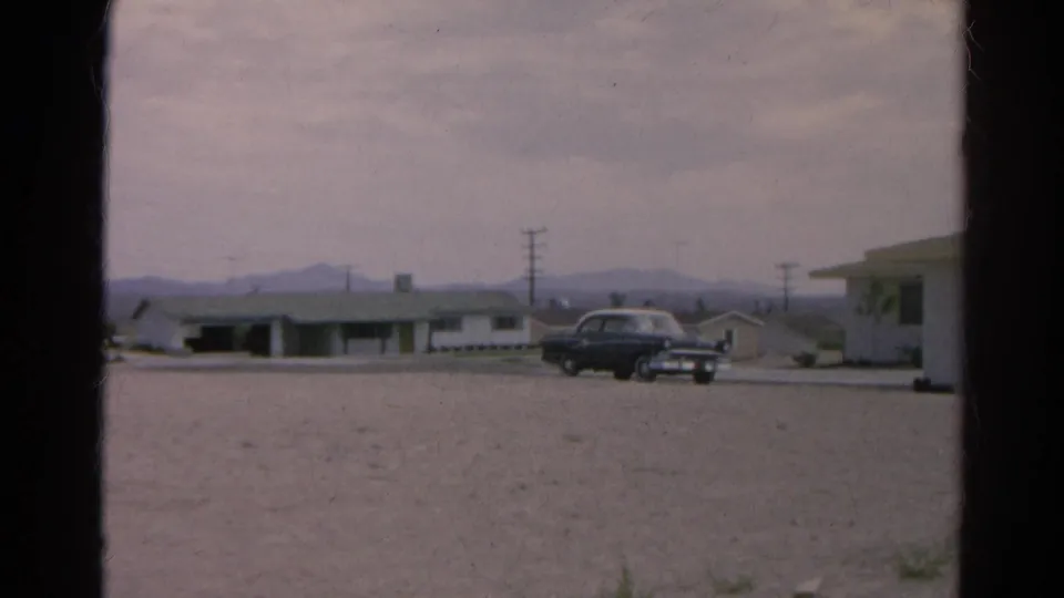 1966 Silver Lake, California roadside scene with a dark sedan, low motel-like buildings, utility poles, gravel foreground, and distant mountains.