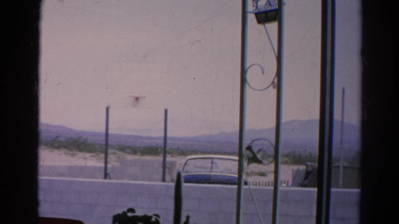 Parked car behind a white wall with distant hills seen through dark window framing.