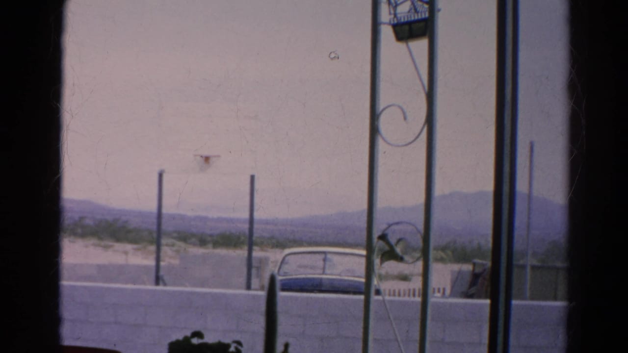 Car roof behind a wall with vertical poles, decorative metalwork, and hazy mountains.