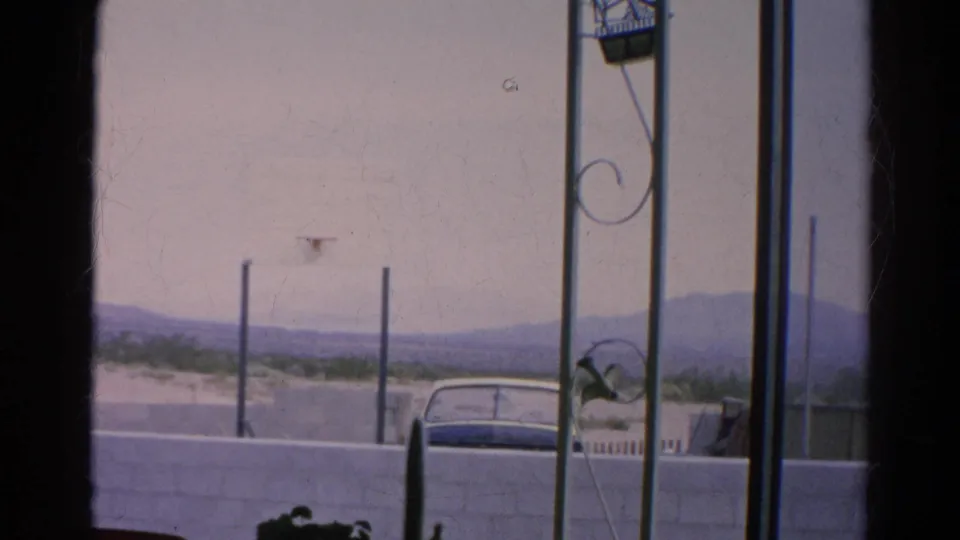 1966 Silver Lake exterior view with a car partly hidden by a block wall, metal porch supports, sparse greenery, and mountains.