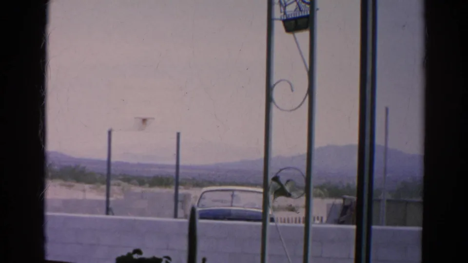 Faded 8mm frame from Silver Lake in 1966 showing a parked car behind a wall and distant hills through a window-like foreground.