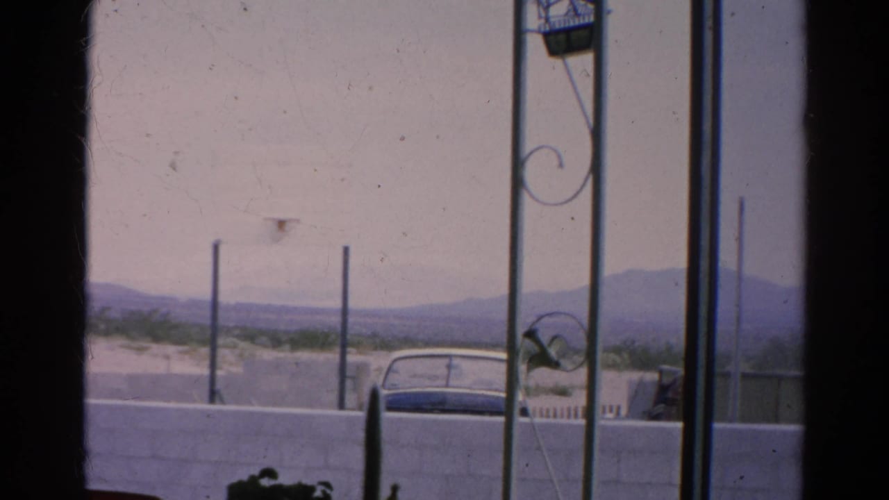 Silver Lake 1966 home-movie frame with a parked car, white wall, ornamental metalwork, sparse vegetation, and low hills.