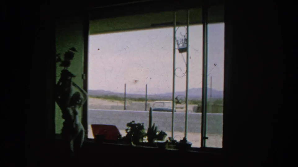 Inside a dim Silver Lake room, silhouetted decor frames a bright street view with a parked car and pale hills in the distance.