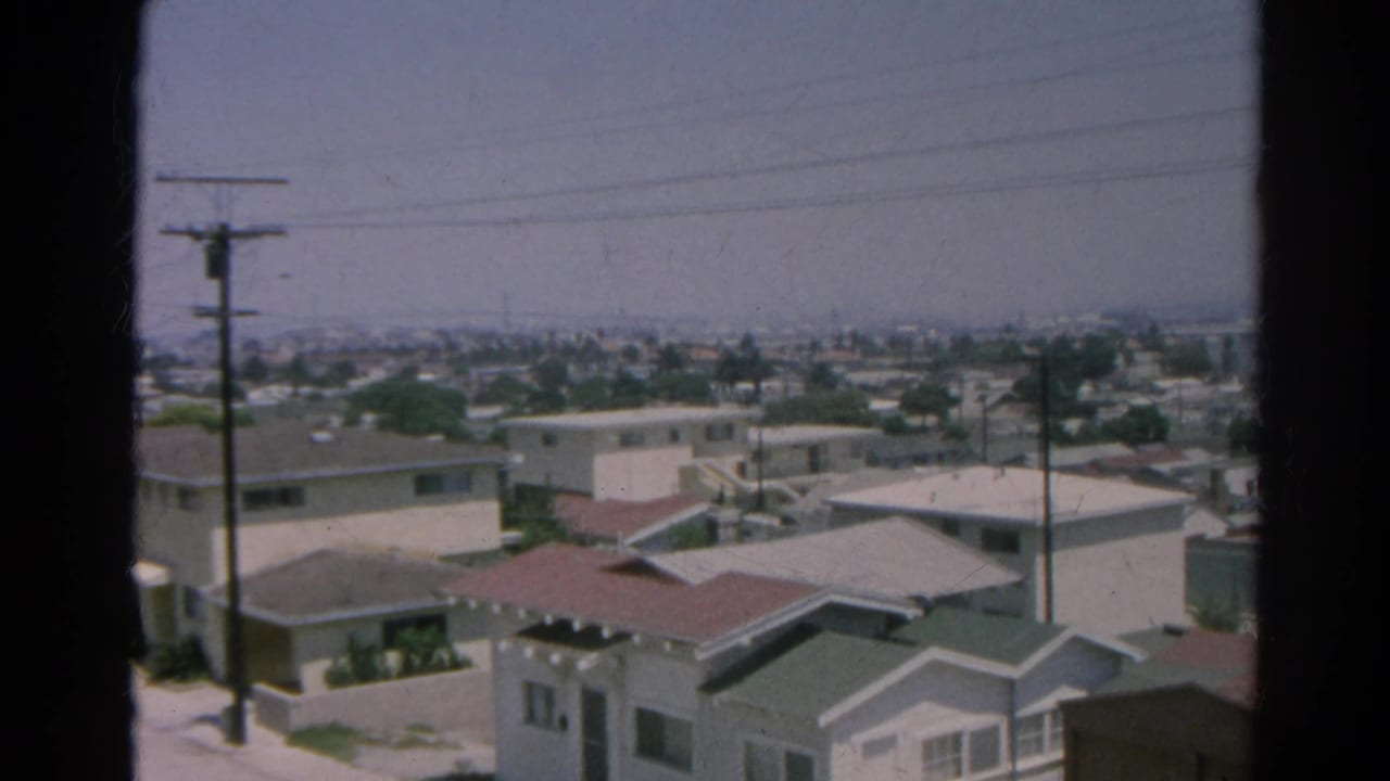 View over pale houses and rooftops with utility poles and a hazy city horizon.