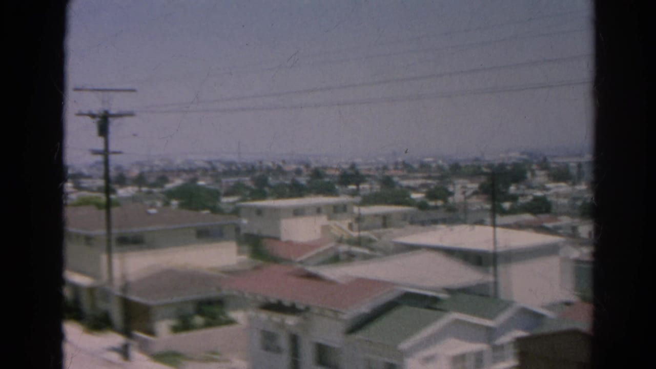 Soft view of closely spaced houses, rooflines, utility poles, and distant urban haze.
