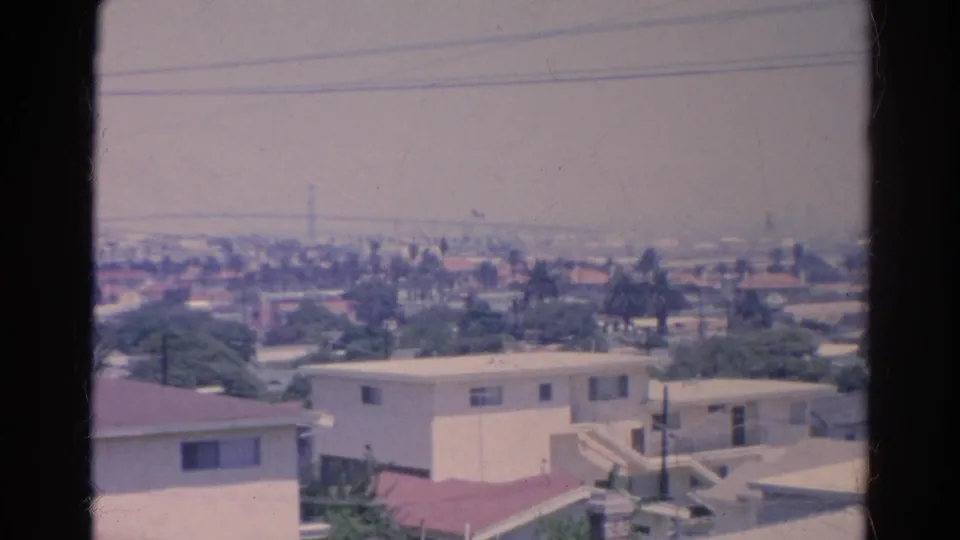 1966 Silver Lake rooftops and pale residential buildings with overhead wires, trees, and distant urban haze.