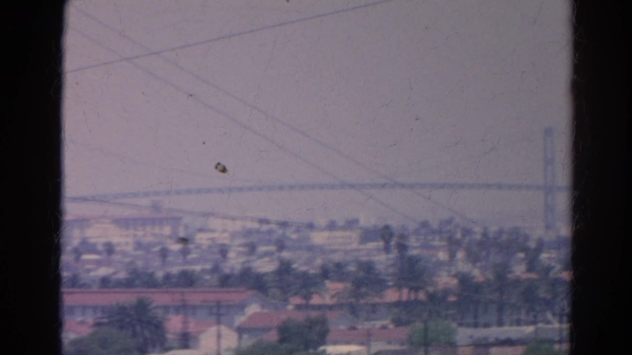 Hazy 1966 Silver Lake-area skyline with palms and rooftops below a distant bridge or elevated span on the horizon.