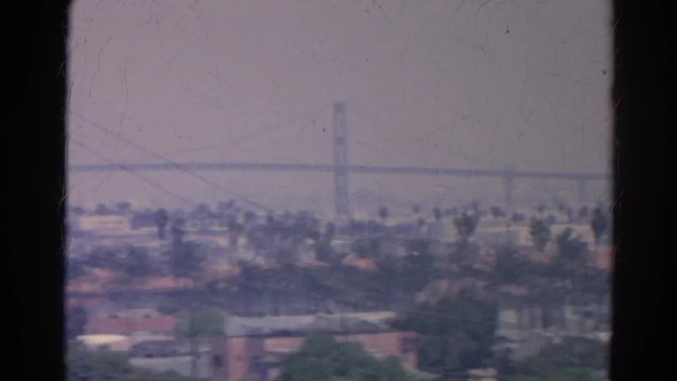 1966 Silver Lake-area urban view with palm-lined blocks, rooftops, a distant vertical tower, and haze softening the background.