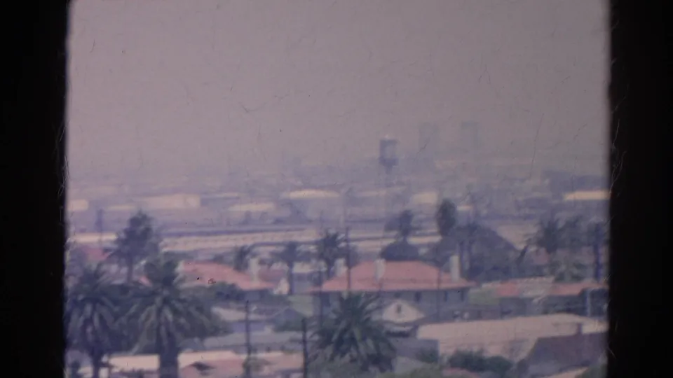 Soft 1966 Silver Lake frame with palms, red roofs, distant structures, and muted color from 8mm film.