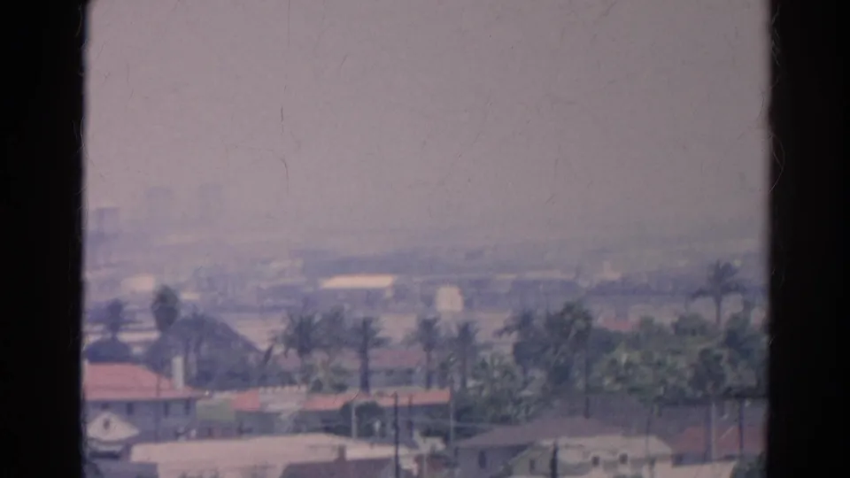 1966 Silver Lake home-movie frame showing red-roof houses, palms, haze, and dark borders from the scanned film.