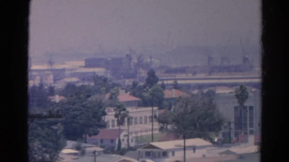 A 1966 8mm view over Silver Lake buildings and trees, with window edges, utility lines, and industrial haze in the background.