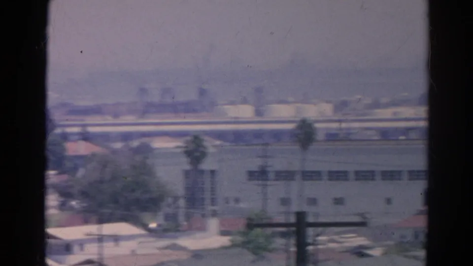 End of the Silver Lake pan showing a pale warehouse, palm trees, roadway or highway lines, and hazy industrial structures beyond.