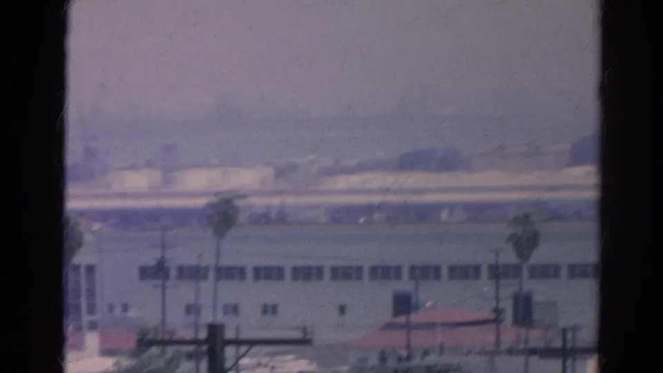1966 Silver Lake view through a window, showing hazy industrial buildings, utility poles, palms, and distant tower forms.