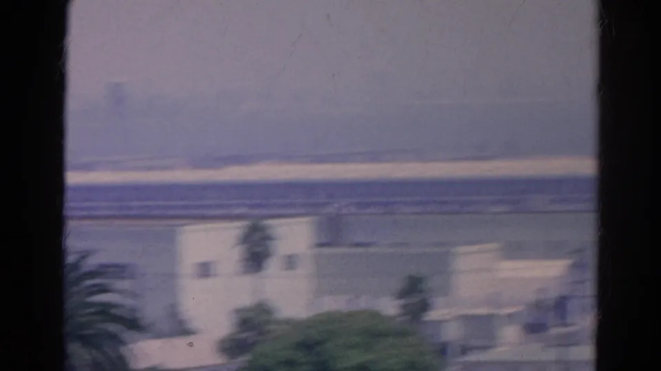 A blurred 1966 Silver Lake frame shows a pale building, palms, and a distant water tower form under a muted sky.