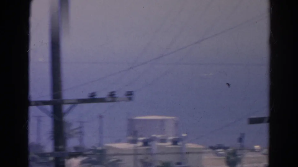 Moving 8mm view in Silver Lake, California, with wires, a roadside pole, palm trees, and soft distant buildings near the horizon.