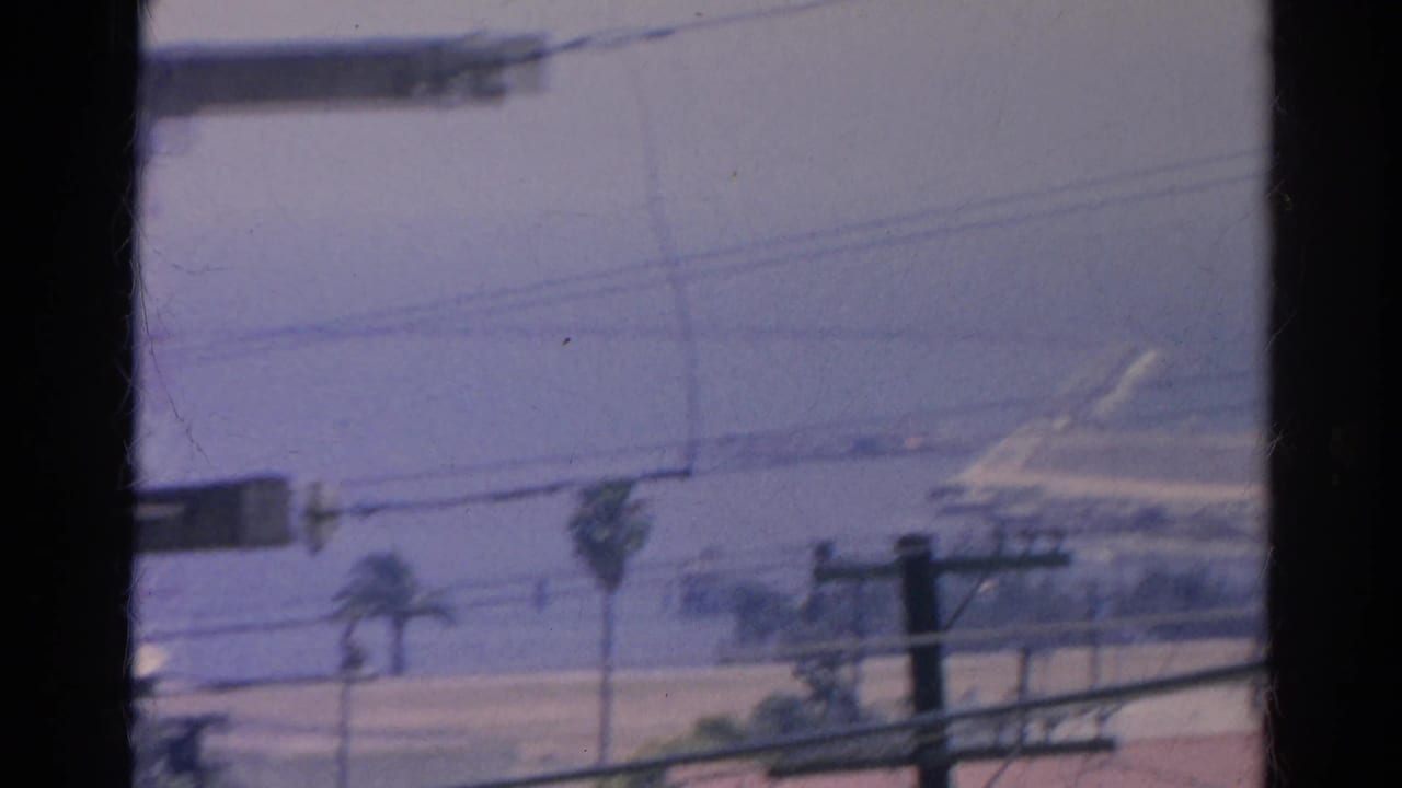 Hazy street view through dark window bars with power lines, palms, and distant rooftops.