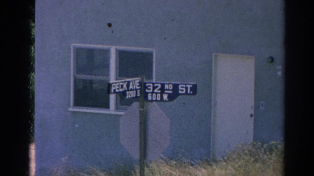Peck Ave and 32nd St signs are centered near a window and plain door on a building facade.