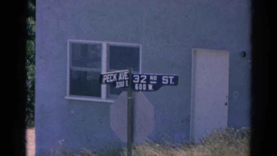 Late frame of the 1966 Silver Lake corner showing Peck Ave and 32nd St signage, doorway, window, and grass.