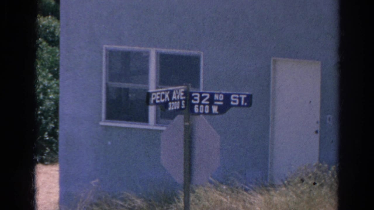 Street signs for Peck Avenue and 32nd Street beside a stucco building.