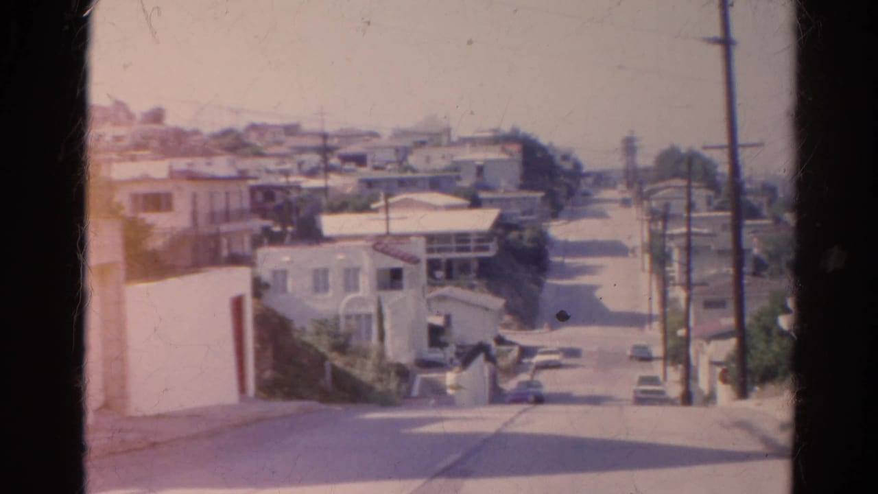Downhill residential street with stucco houses, parked cars, and utility poles.