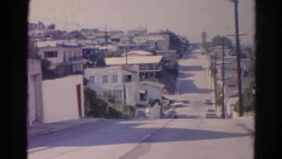 1966 Silver Lake street view with a steep residential roadway, stucco houses, parked cars, utility poles, and visible film-frame edges.