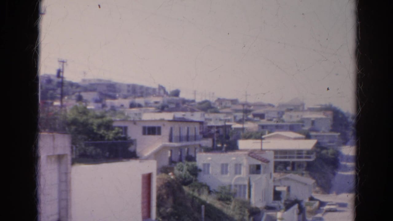 Hillside residential view with white houses, greenery, utility poles, and distant ridgeline.