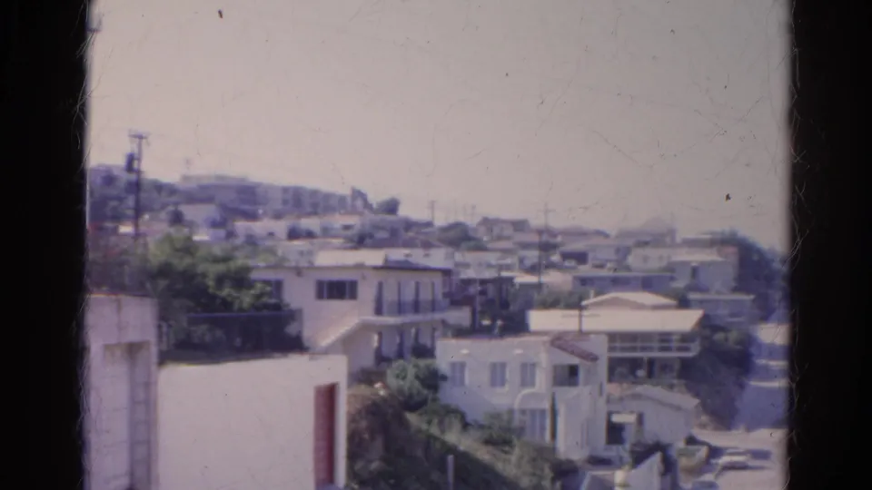 1966 Silver Lake hillside view with stucco homes, plants, utility poles, and a hazy ridge in the distance.
